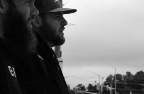 lack-and-white image of two Hip-Hop artists, Legit and HostileProd, standing side by side on a city street, wearing caps and looking forward, capturing a gritty, cinematic underground Hip-Hop aesthetic