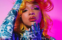 Ultra-realistic image of a vibrant female Hip-Hop artist reading fan comments on her phone in a colorful studio environment, symbolizing the modern comment economy where fan conversations influence which songs become hits — SpitFireHipHop Corporate Corner.