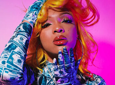 Ultra-realistic image of a vibrant female Hip-Hop artist reading fan comments on her phone in a colorful studio environment, symbolizing the modern comment economy where fan conversations influence which songs become hits — SpitFireHipHop Corporate Corner.