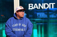 Hip-Hop artist wearing a hoodie stands near a window at night with city lights in the background, creating a reflective mood for the “So We Loved Ourselves” visual.