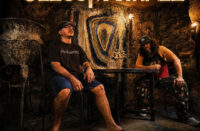 Jezus Martinez pose inside a dimly lit room with glowing gold typography promoting their EP THE SALAMANDER and the single “Hall of Mirrors.”