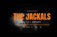 The Jackals cover art by Mic Bles and Avant Garde featuring bold orange title text, black noir-inspired background, smoke effects, and lion-versus-jackals thematic imagery.