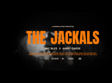 The Jackals cover art by Mic Bles and Avant Garde featuring bold orange title text, black noir-inspired background, smoke effects, and lion-versus-jackals thematic imagery.