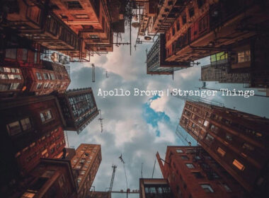 Cover artwork for Apollo Brown's instrumental single "Stranger Things," featuring an upward-looking view between towering city buildings with a cloudy sky centered above, creating an atmospheric and cinematic perspective.