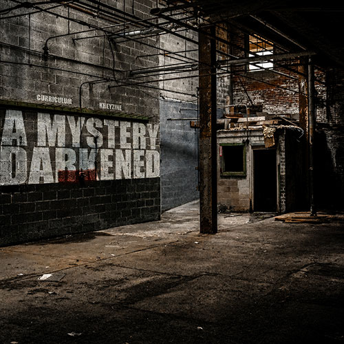 Curriculum and KHEYZINE A Mystery Darkened album cover featuring a shadowy abandoned industrial building with the album title painted across a concrete wall.